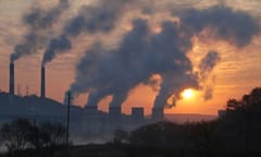A photo of a line of smokestacks belching smoke into the atmosphere at sunset