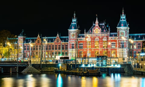 Long exposure night photograph of Amsterdam Central Station with stunning lighting against a dark sky, showcasing the beauty of the iconic architecture.